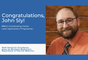 John Sly has medieum-brown hair and a beard and wears glasses, an orange button-down shirt, and striped tie.