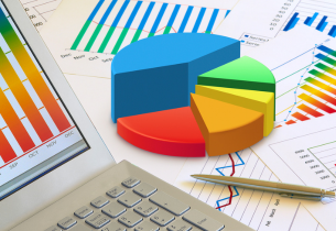 A variety of colorful reports are on a laptop screen and table top.