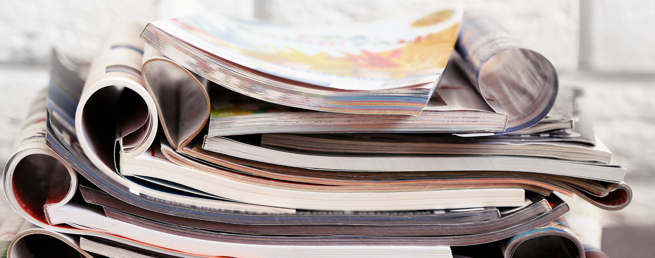 A stack of medical journals sits on a table in front of a white brick wall.