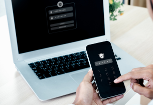A person sits at a laptop using a phone for two-factor authentication.