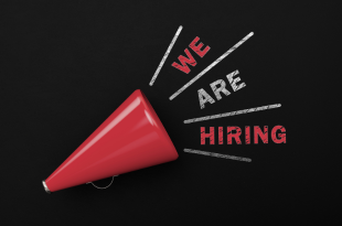 A red megaphone is on a black background with the words "we are hiring" written in red and white chalk.
